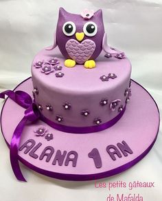 a purple cake with an owl on top and name written in spanish, sitting on a pink plate