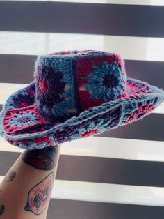 a woman's hand holding a crocheted hat in front of a window