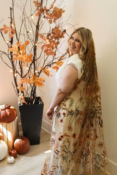 a woman is standing in front of a tree with pumpkins and lights on it