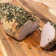 a piece of meat with herbs on it sitting on a cutting board next to a knife