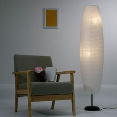 a white lamp sitting next to a chair with a laptop on it's lap