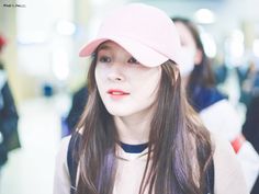 a woman with long hair wearing a pink hat and looking at the camera while standing in an airport