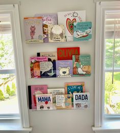 several books are hanging on the wall in front of two windows with white trimmings