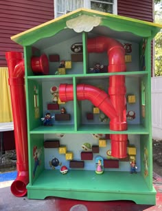 a green and red toy house with pipes coming out of it's roof to the side