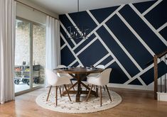 a dining room table with white chairs in front of a blue and white geometric wall