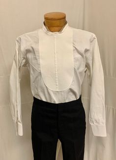 "1900, 15\" Neck, linen collarless shirt with pique front bib, with 3 stud button holes.  Shirt buttons  down back. Curved at each hip at Nottoway.  Sleeves are long and double French cuffs. Label reads Brook Brothers made in England. Measurements: neck 15\" Chest 44\" Shoulder to shoulder 17\" Shoulder to hem 31\" Sleeves 25\" Arm holes 9\" Mid section 44\" Condition excellent" Classic Stand Collar Tops With Buttons, Classic Shirt With Stand Collar And Placket, Traditional Fitted Shirt With Buttons, Classic Formal Tops With Stand Collar, Classic Semi-formal Top With Stand Collar, Classic Shirt With Stand Collar And Buttons, Fitted Dress Shirt With Buttons For Daywear, Classic Tops With Stand Collar And Button Cuffs, Classic Tops With Button Cuffs And Stand Collar