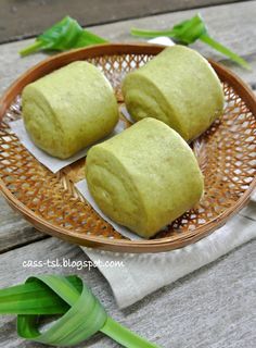 three green rolls sitting on top of a wooden plate next to some leaves and napkins