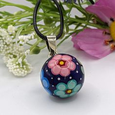 a blue and pink flowered glass ball on a black cord necklace with flowers in the background