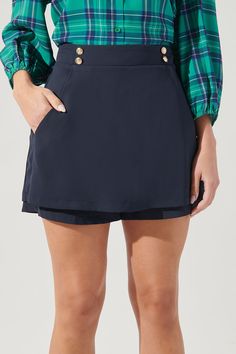 Set sail in this nautical skort! Sitting high on the waist, it features a double button detail along each side of the waistband. It maintains a trapeze silhouette with a skirt overlay against shorts that peak through. The backside maintains the same shape with added elastic at the waist, along with a zipper for easy accessibility. Easily pair it with your favorite top and loafers for a clean cut look.- Decorative buttons- Pockets- Elastic waistband- Zipper- Color: NavySize + Fit - Model is 5'9" Preppy Short Lined Skirt, Navy Skort For Workwear, High Waist Lined Skort In Preppy Style, Preppy High Waist Lined Skort, Chic Short Skort With Buttons, High Waist Preppy Skort With Lined Skirt, Preppy Skort For Workwear With Lined Skirt, Preppy Lined Skort For Workwear, Preppy Skort With Lined Skirt For Work