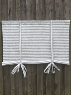 a white window curtain hanging on the side of a wooden fence with two ties tied around it