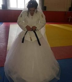 a woman in a white wedding dress is standing on a blue mat with a black belt around her waist