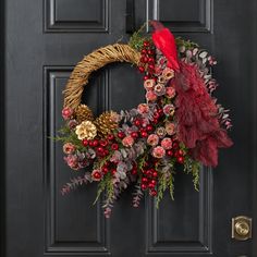 a wreath with feathers, berries and pine cones is hanging on the front door handle