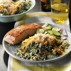 a white plate topped with salmon and rice next to a bowl of vegetables on a table