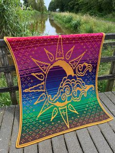 a colorful quilt on a wooden deck overlooking a river and trees in the background,