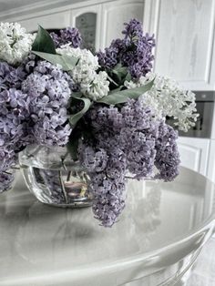 a vase filled with purple and white flowers on top of a table in front of a mirror