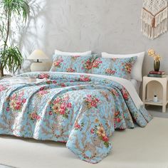 a bed covered in blue and pink flowers next to a white table with a plant