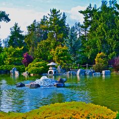 a pond surrounded by trees and rocks in the middle of a park with lots of flowers