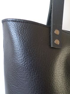 Large everyday casual vegan leather tote bag in black with real leather handles. * Exterior: - High quality vegan/faux leather in black color. * Interior: - Charcoal gray Italian natural cotton. * Two inside slip pockets for personal belongings like phone, keys, etc. * Real leather handles in black attached with antique toned brass rivets * Closes with magnetic snap closure reinforced with natural leather * Additionally lined for better structure. Measurements: Height: 15 inches Width of the bag Modern Black Textured Leather Shoulder Bag, Black Double Handle Bucket Bag For Work, Black Leather Bucket Bag For Work, Everyday Recycled Leather Shoulder Bag With Leather Lining, Everyday Bucket Bag With Double Leather Handles, Minimalist Shoulder Bag With Leather Handles For Everyday, Modern Shoulder Bag With Leather Lining For Everyday Use, Modern Everyday Shoulder Bag With Leather Lining, Modern Black Shoulder Bag With Leather Backing