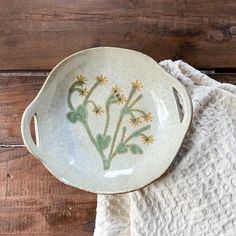 a dish with flowers painted on it sitting on top of a white towel next to a wooden table