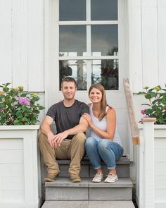 a man and woman sitting on steps in front of a white building with flowers outside