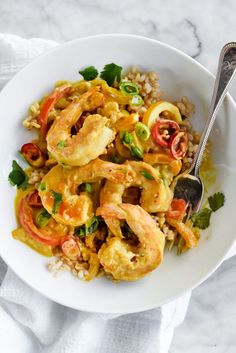 a white bowl filled with shrimp and rice on top of a marble table next to a silver spoon