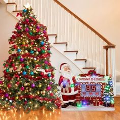 a decorated christmas tree sitting in front of a stair case next to a santa clause