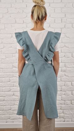 a woman standing in front of a brick wall wearing a blue vest with ruffles