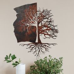 a metal tree with its roots in the shape of a human head on a wall next to a potted plant