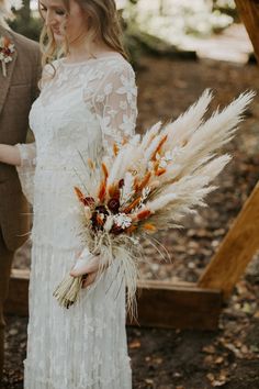 a bride and groom standing in the woods holding their bouquets with dried flowers on them