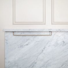 a white marble counter top with brass handles in front of a wall mounted cabinet door