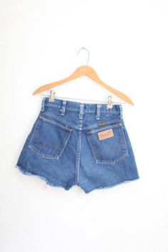 maker: wrangler material: cotton used  vintage condition. raw hemline actual measures: waist:26" thigh: 11" across hips:20" across rise:12" inseam:2" total length:14" Retro Cotton Jean Shorts With Frayed Hem, Vintage High-rise Dark Wash Jean Shorts, Vintage Dark Wash Mid-rise Shorts, Vintage Style Mid-rise Dark Wash Shorts, Retro Cotton Shorts With Frayed Hem, Vintage Cotton Shorts With Frayed Hem, Vintage Dark Wash Jean Shorts, Vintage High-waisted Dark Wash Jean Shorts, Vintage Dark Wash Shorts