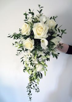 a bouquet of white roses and greenery is held by someone's hand against a wall