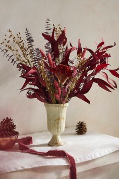 a white vase filled with red flowers on top of a table next to a pine cone