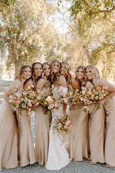 a group of women standing next to each other holding bouquets in front of trees