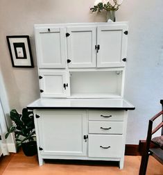 a white hutch with black handles and drawers next to a chair in a room