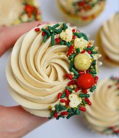 cupcakes decorated with icing and decorations are being held by someone's hand