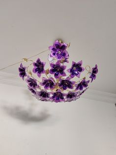 a purple flowered glass crown hanging from the ceiling in front of a white wall