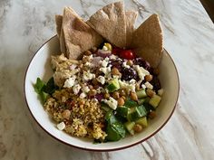 a white bowl filled with salad and tortilla chips on top of a marble counter