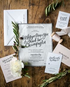 the wedding stationery is laid out on a wooden table with flowers and greenery