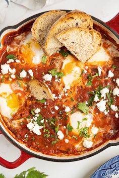 an iron skillet filled with baked eggs and tomato sauce, bread on the side