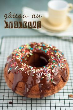 a chocolate donut with sprinkles on a cooling rack next to a cup of coffee