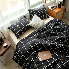 a black and white comforter on a bed in a room with a table, lamp and window