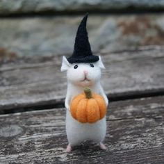 a small white mouse with a black hat and orange pumpkin in it's hand