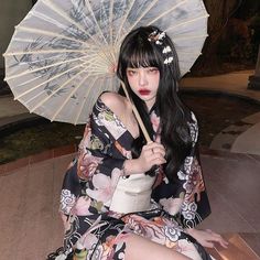 a woman sitting on the ground with an umbrella in her hand and wearing a kimono