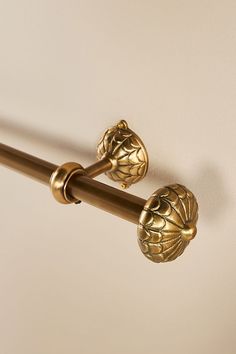 two gold handles on a white wall and a brown curtain rod with decorative leaves attached to it