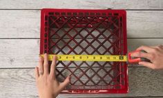 someone is measuring the width of a red basket with a tape on it and another person's hand