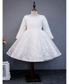 a white dress on a mannequin stand next to a vase with flowers in it