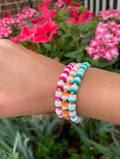 a woman's arm with colorful bracelets and flowers in the backgroud