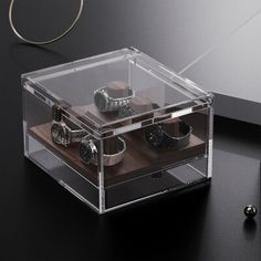 an acrylic box with watch parts in it on a table next to other items