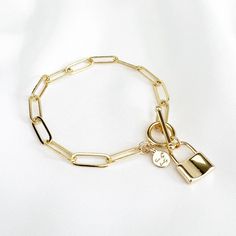 a close up of a gold bracelet on a white surface with a key and lock